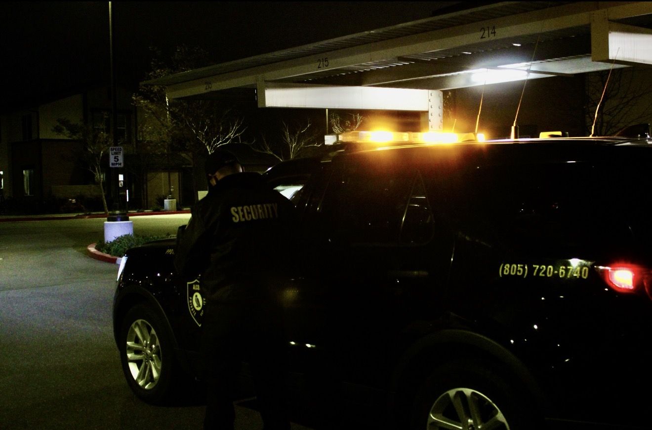 Officer in a Security jacket at the patrol SUV at night, amber light bar on