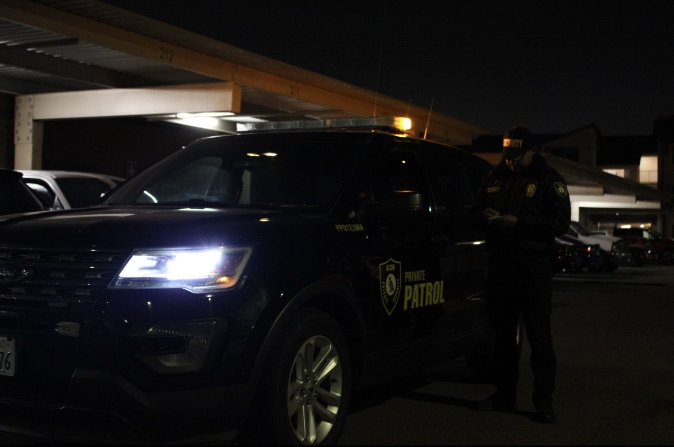 Officer checking notes next to an Alcon patrol vehicle under a carport at night